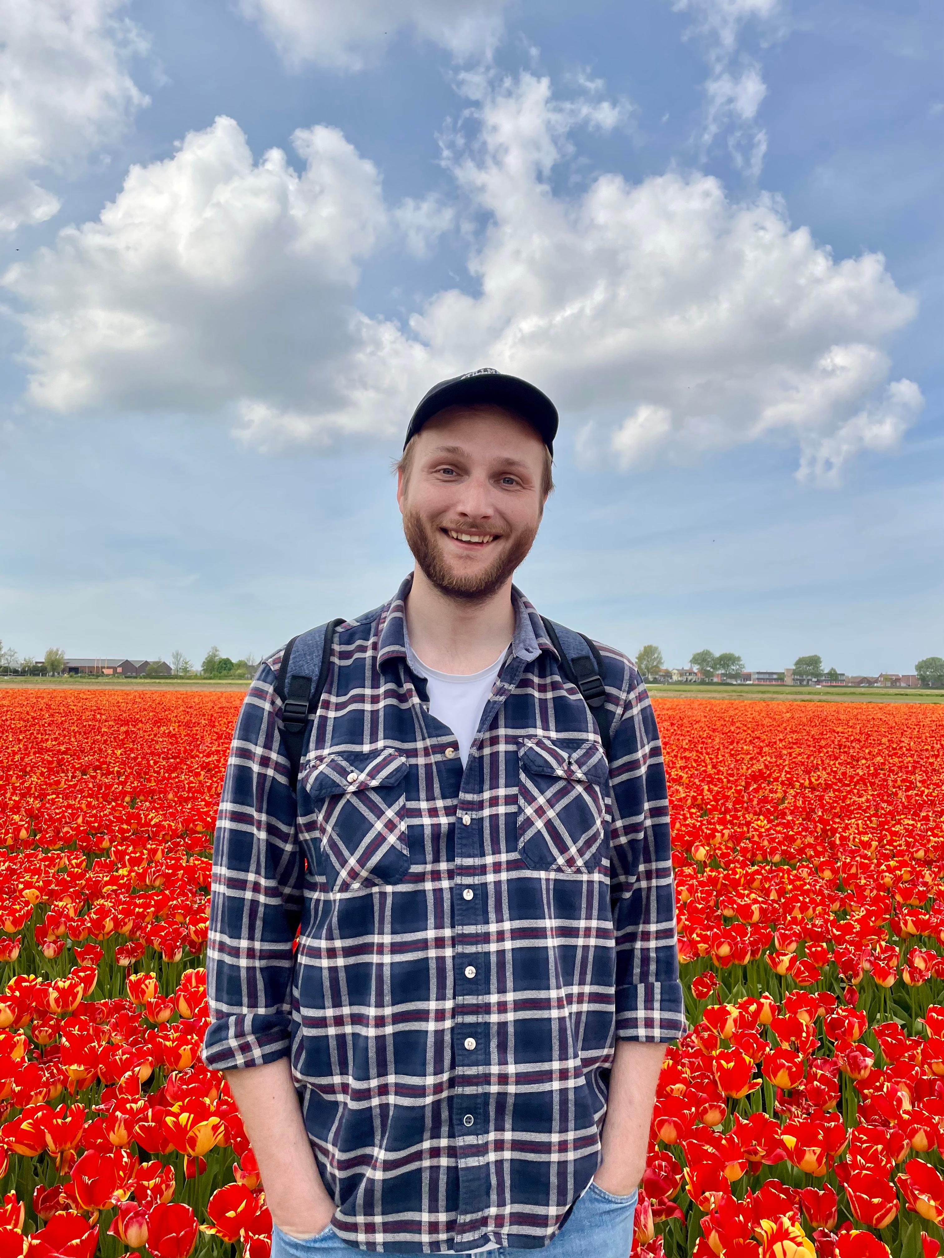 Patrick wearing blue shirt and a hat in front of a field of red tulips